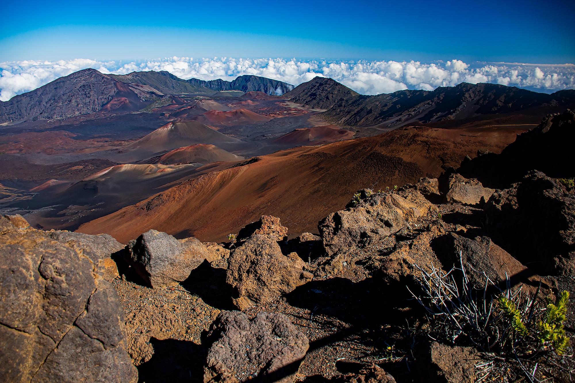 Various hues of reds, oranges, blacks, yellows across a hilly volcanic landscape and a blue sky in t