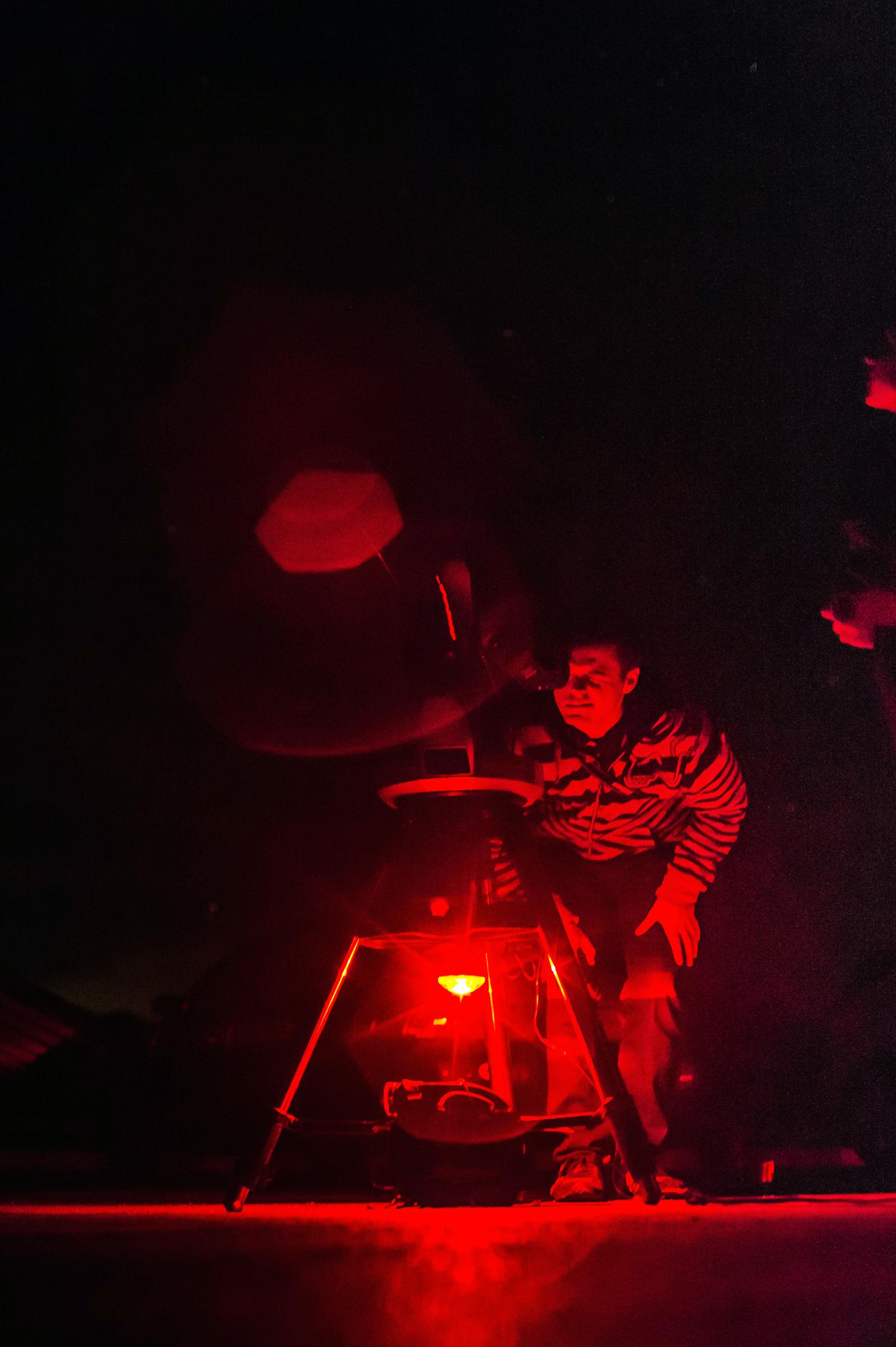 Illuminated in red, a visitor looks through a telescope at night