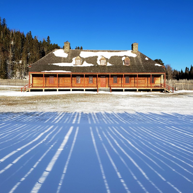 A historic wood building with long shadows cast by a stockade.