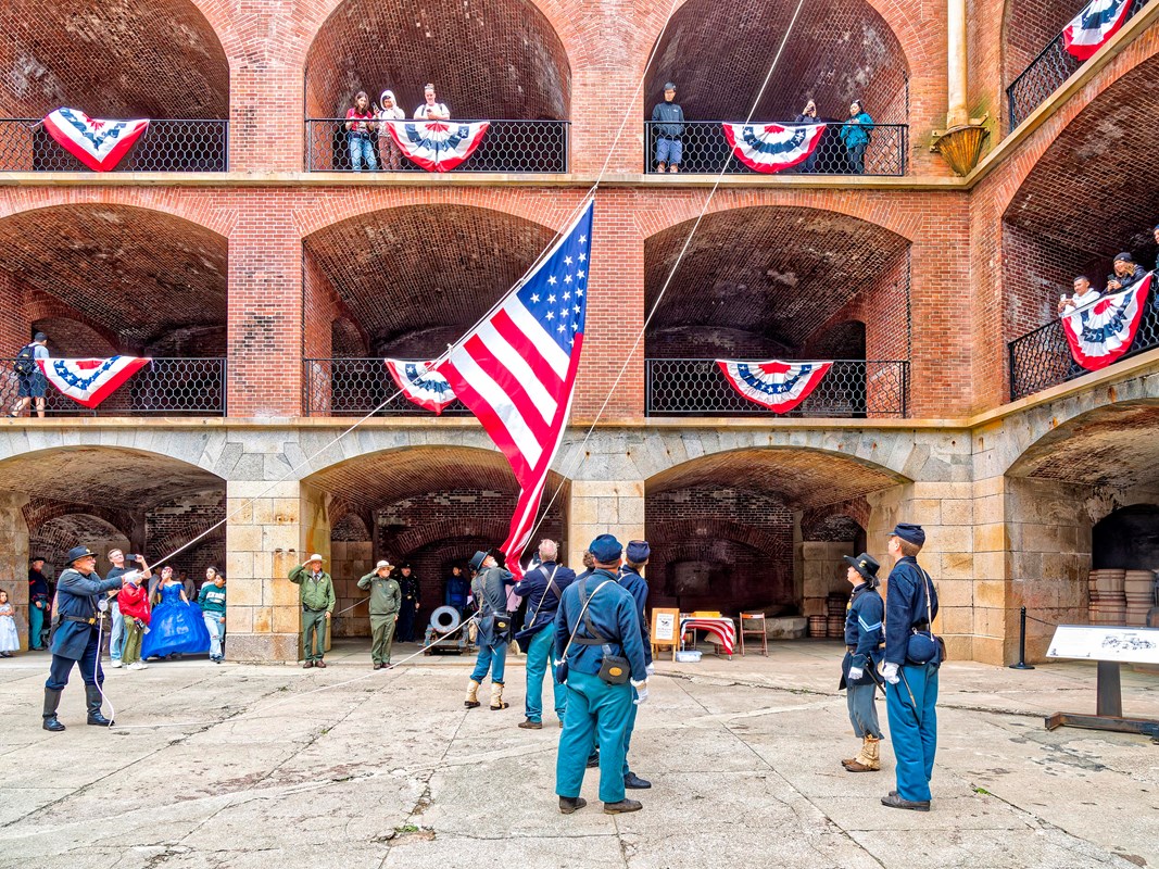 Civil War era reenactors lower the flag inside Fort Point NHS with visitors watching.