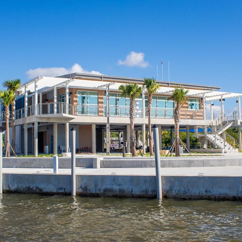 A visitor center building on stilts with dark water in front of it and palm trees around it.