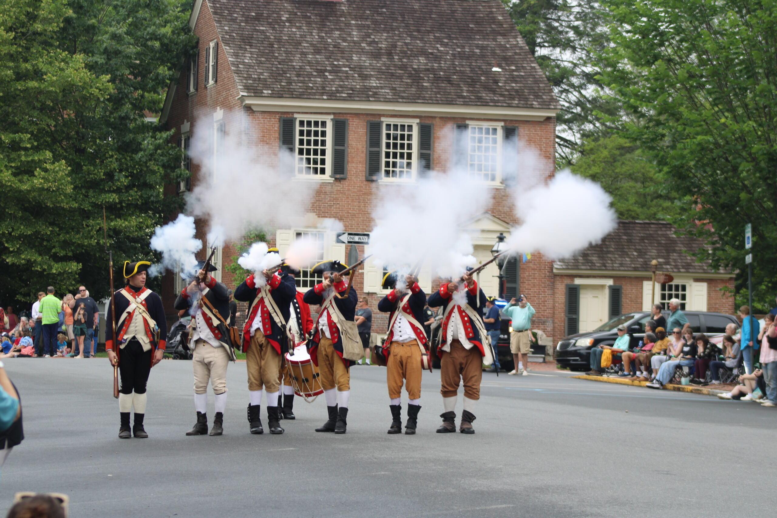Men in colonial outfits fire weapons.