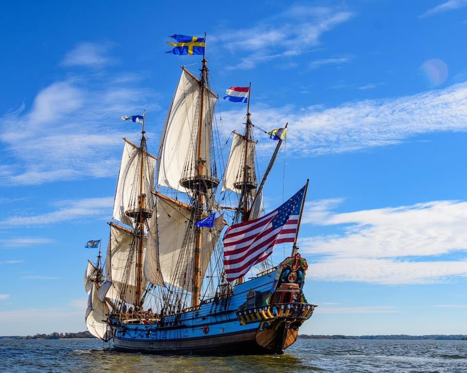 A blue and yellow tall sail ship sails on open water.