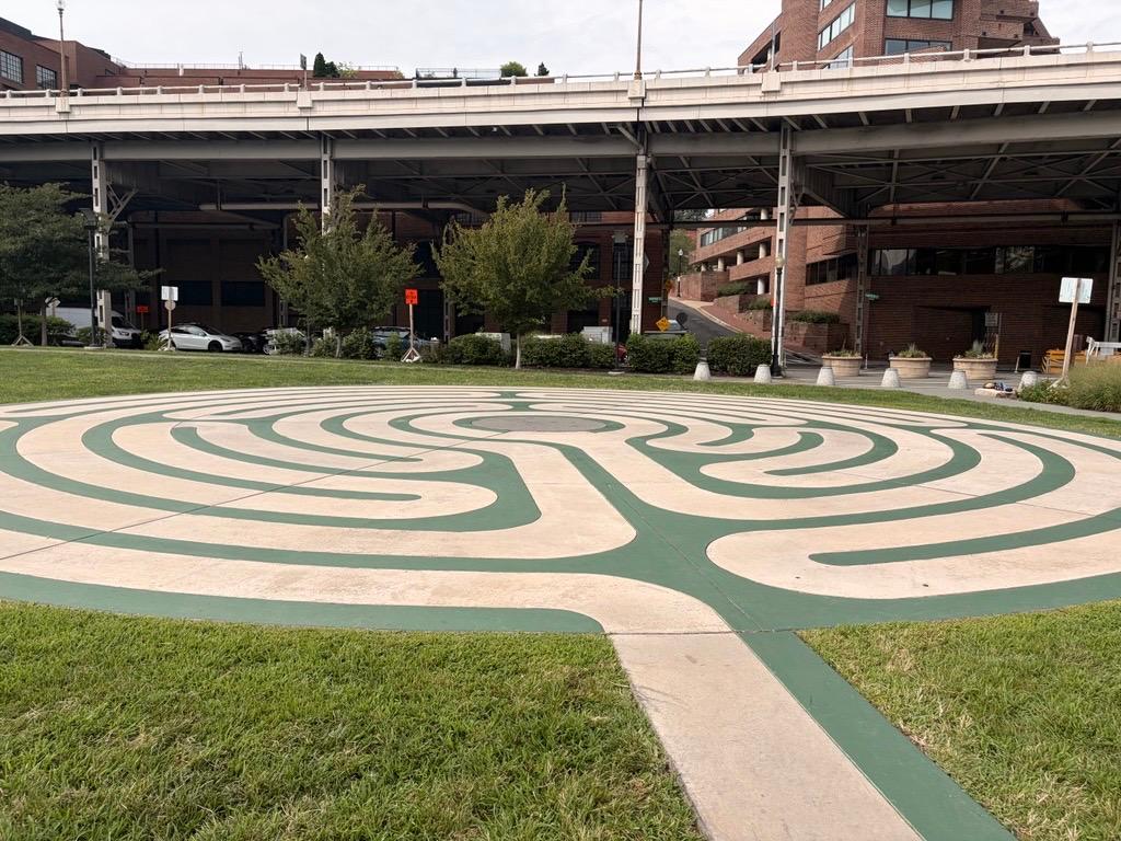 a large concrete painted labyrinth on the lawn with a highway overpass behind it