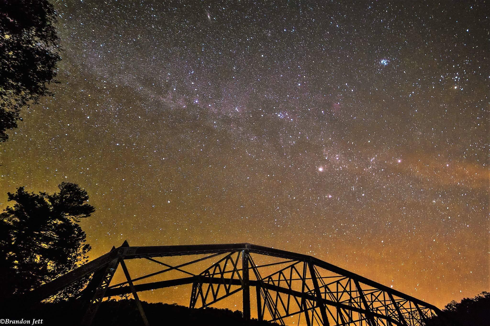 A starry night sky over the silhouette of an iron truss bridge
