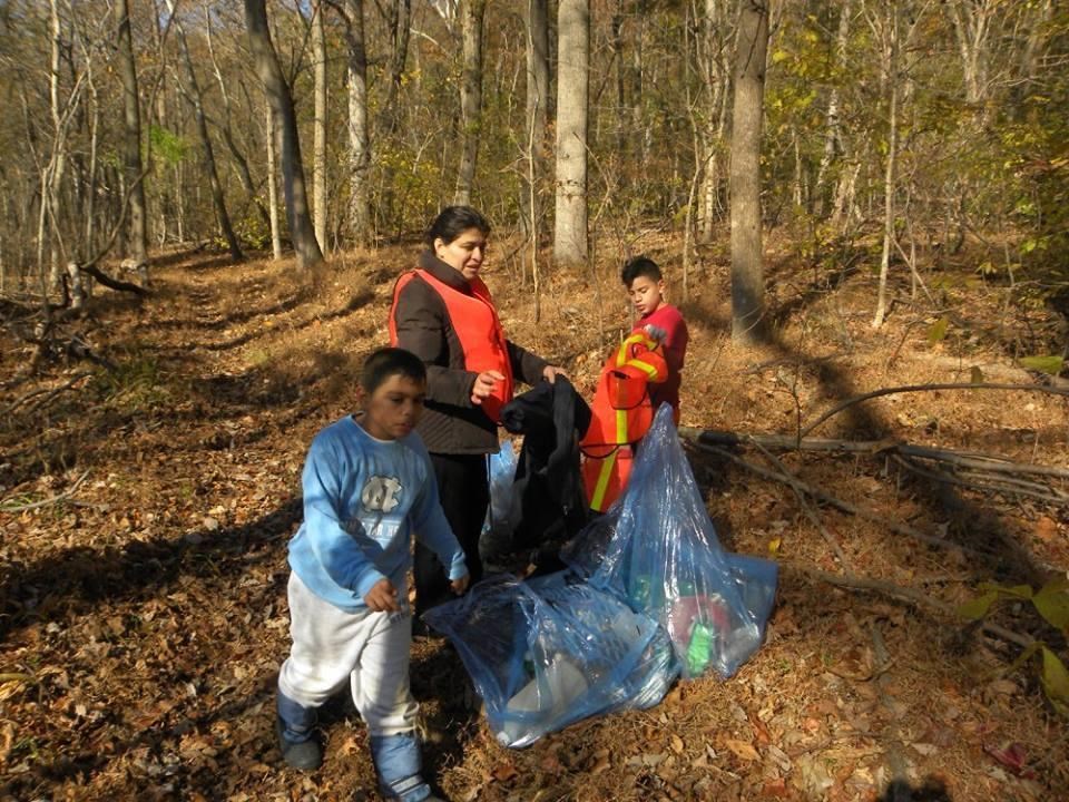 two adults and a kid with trash bags collect trash in the woods