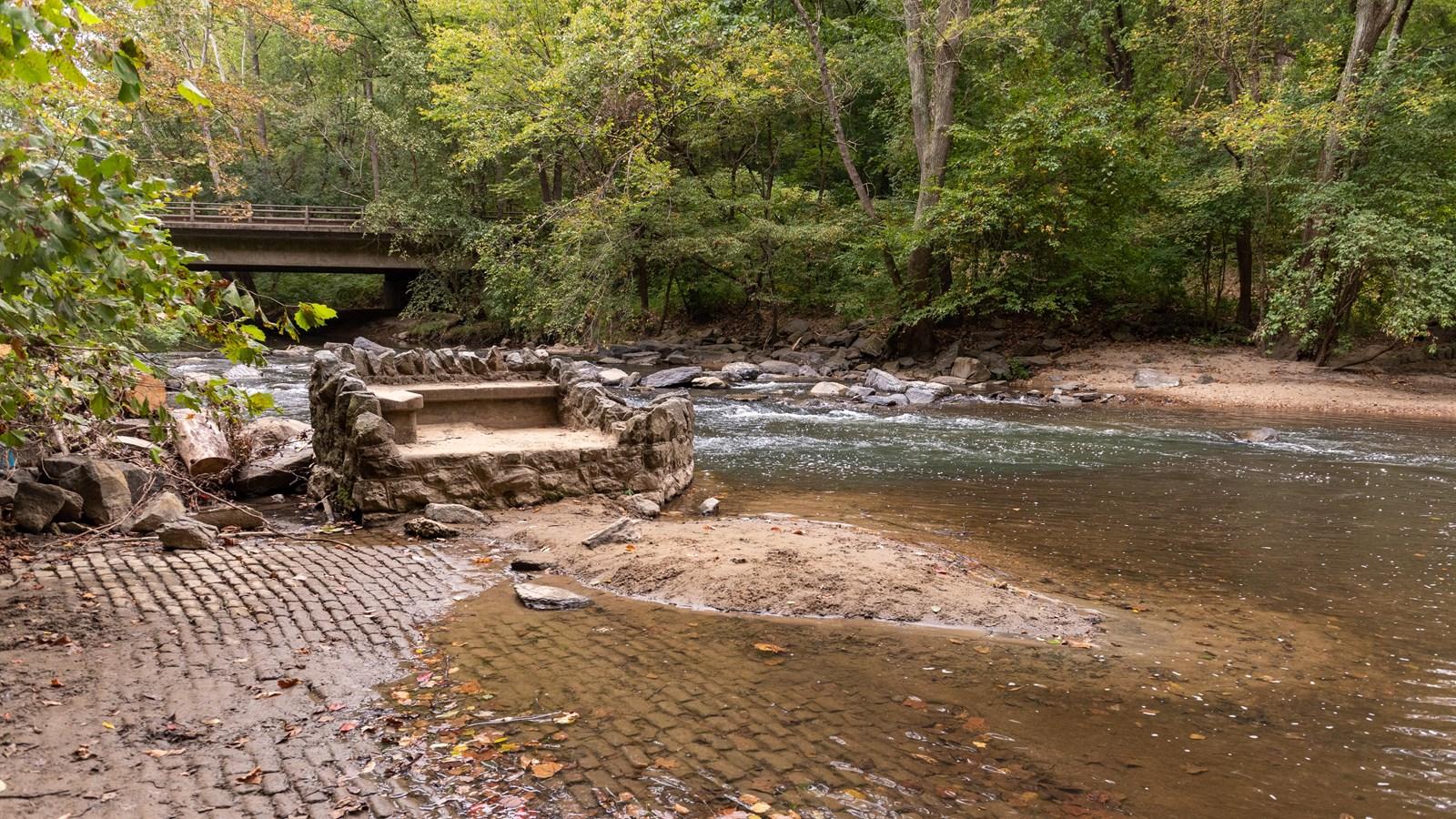 Remnants of a brick road, with historic viewing bench along the shores of Rock Creek. In the distanc