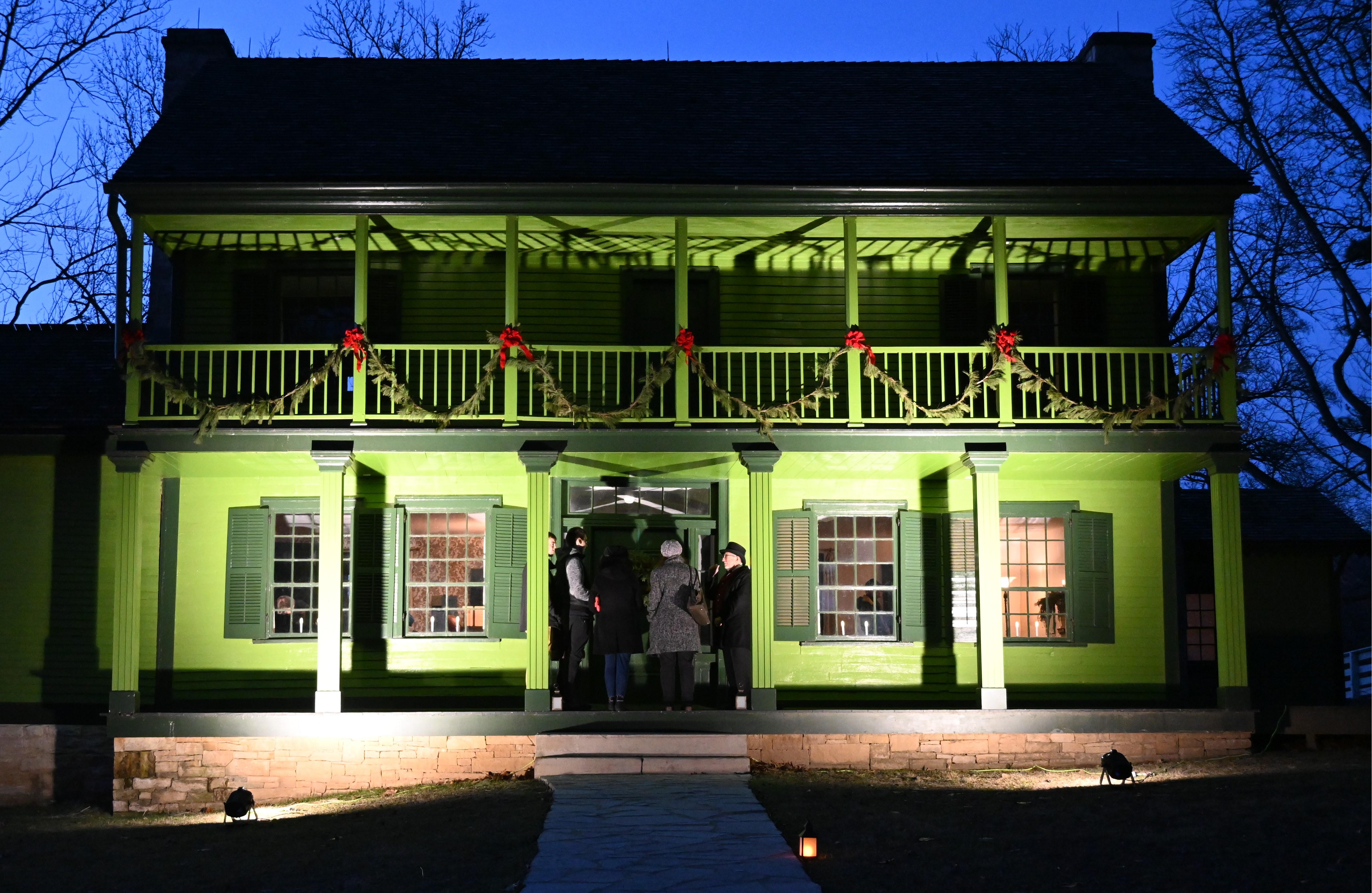 picture of green house at night with pine roping and red bows on balcony