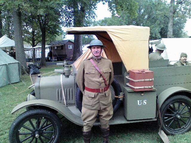 Man dressed on World War I uniform in front of a WWI vehicle.