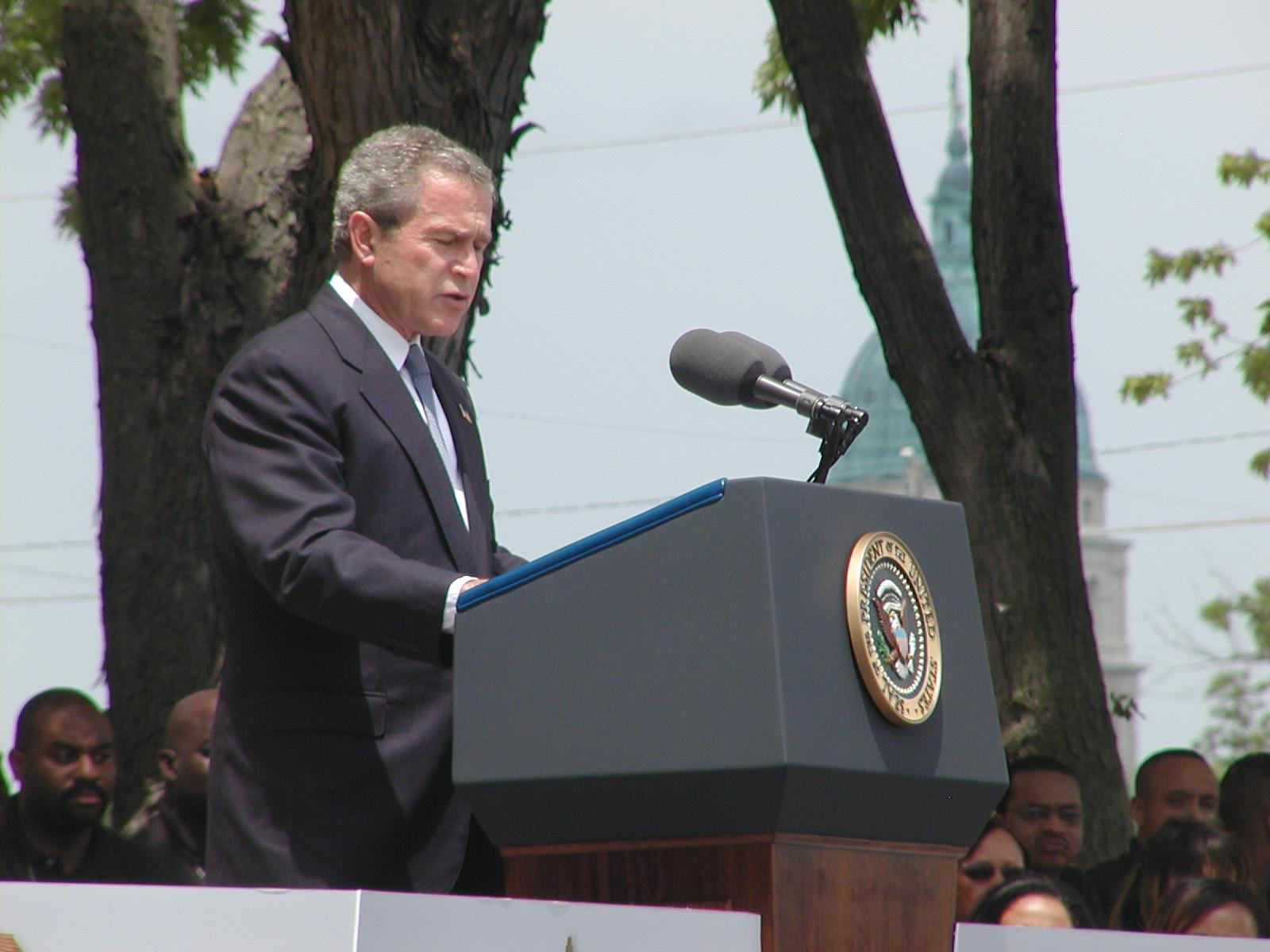President George W. Bush speaks in front of Monroe School with the Kansas State Capitol behind
