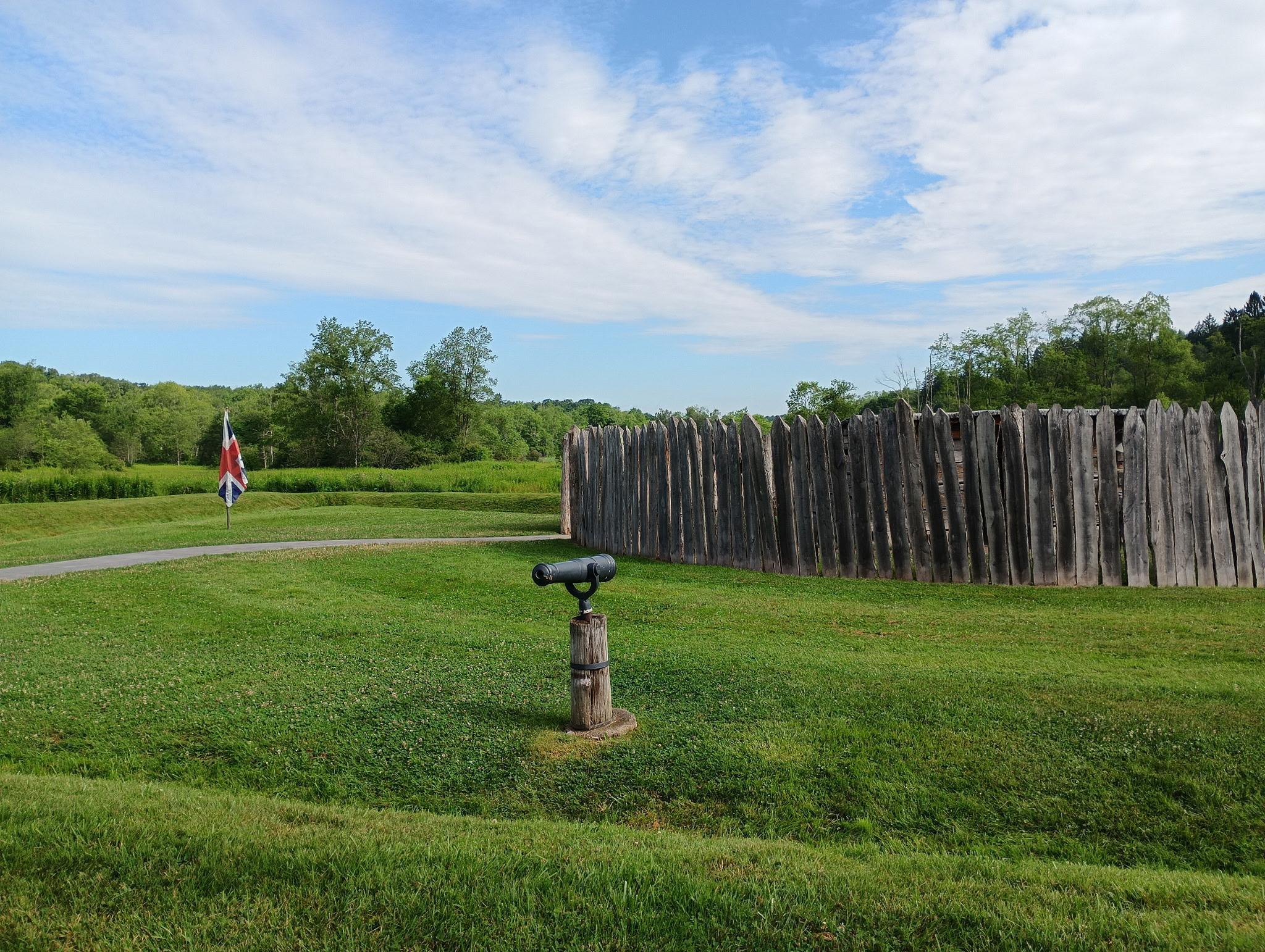 Image of a small circular stockcade fort and earthen mounds around it with a small black cannon