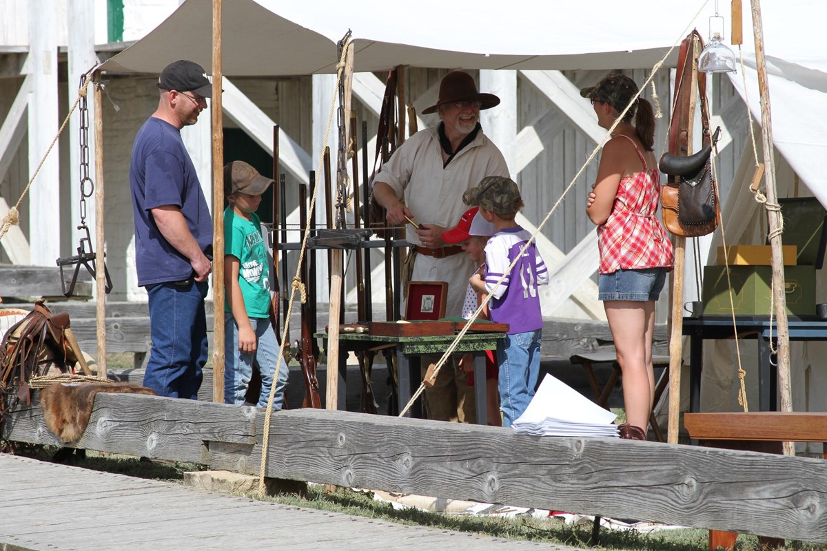 Reenactor in period clothing talks to a family in tent