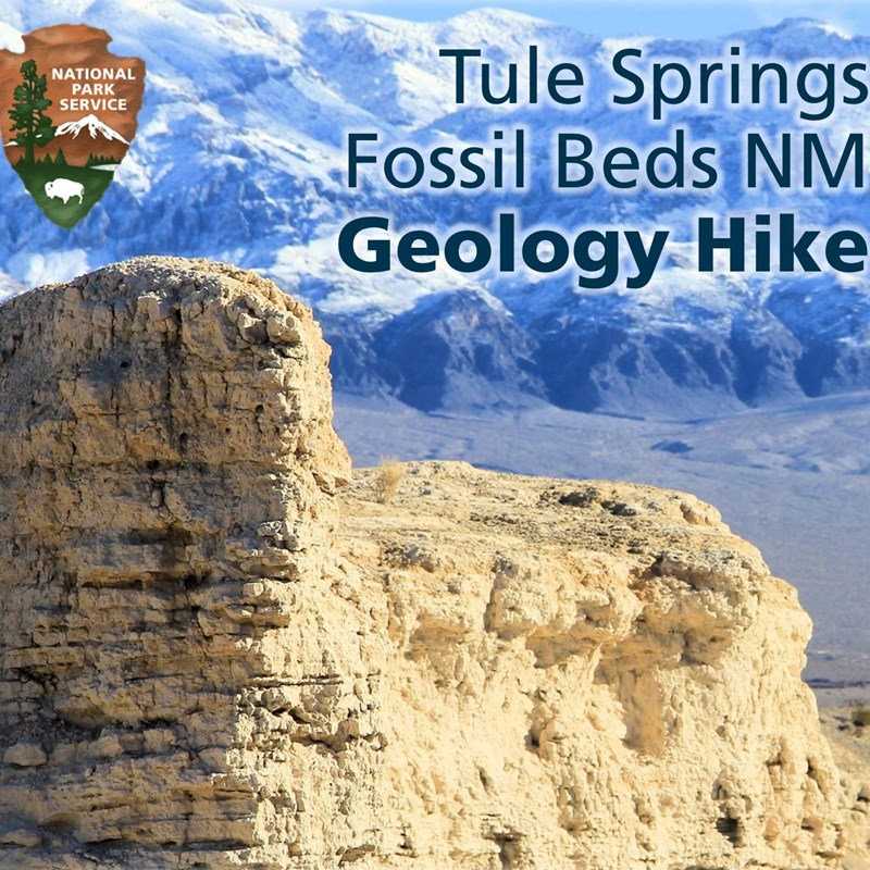 A photo of tan badlands against the backdrop of a snowy Las Vegas Range.