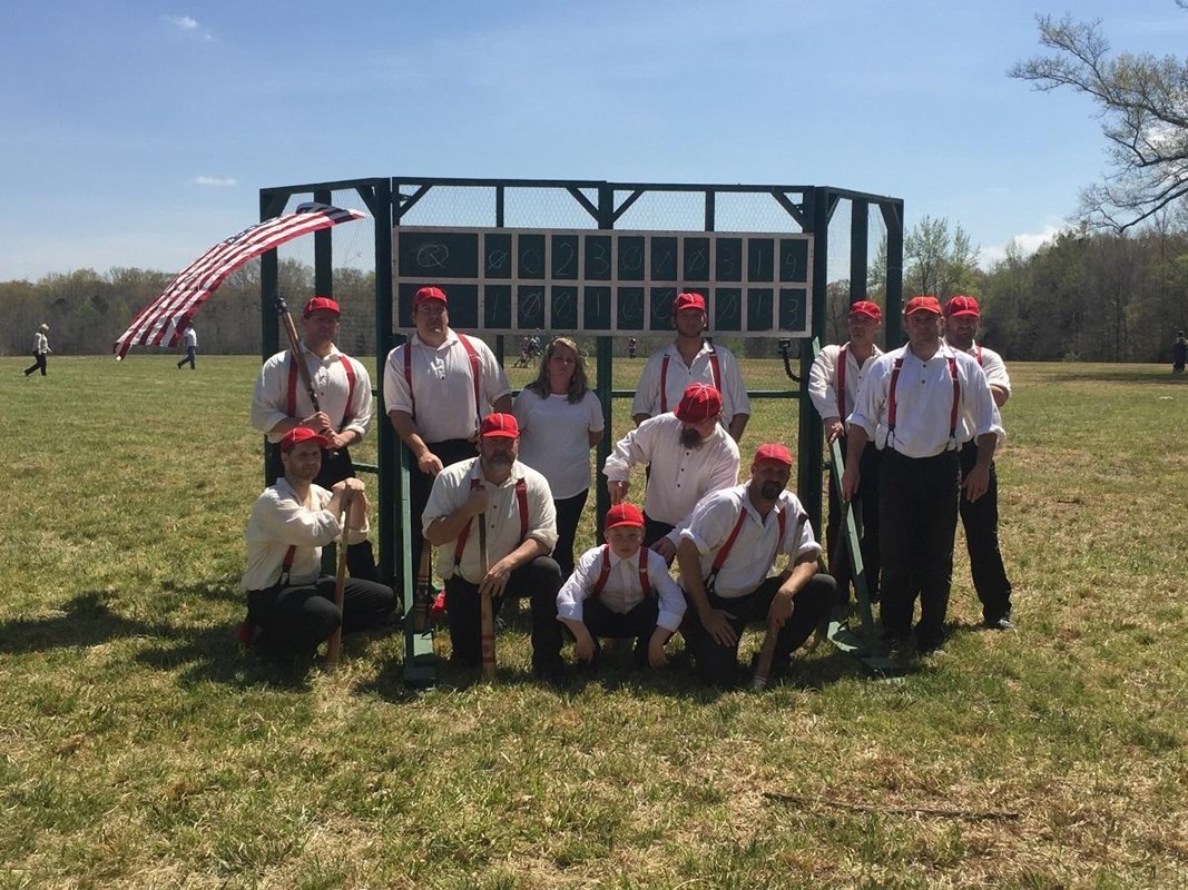 Players in vintage uniforms pose in front of period backstop