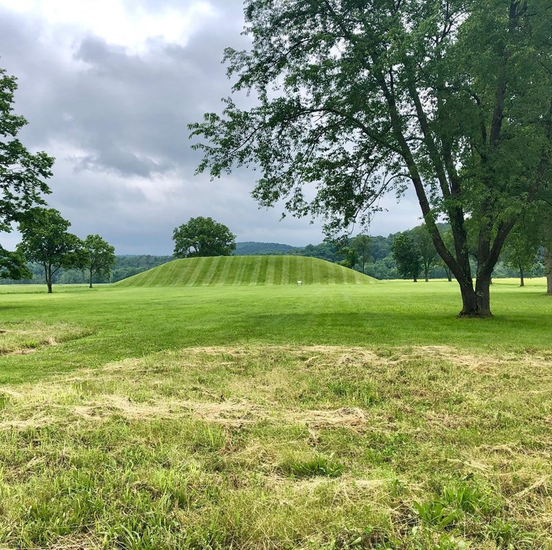 a large earthwork mound sits in a grass field.