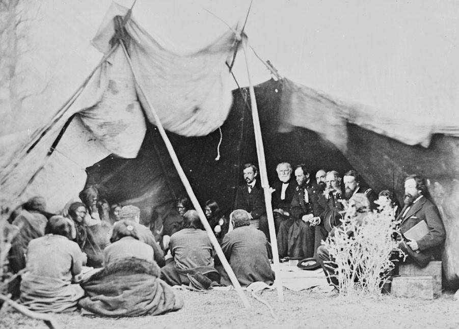 Native and European American men sit under a rain fly in 19th century clothing with Gen Sherman.