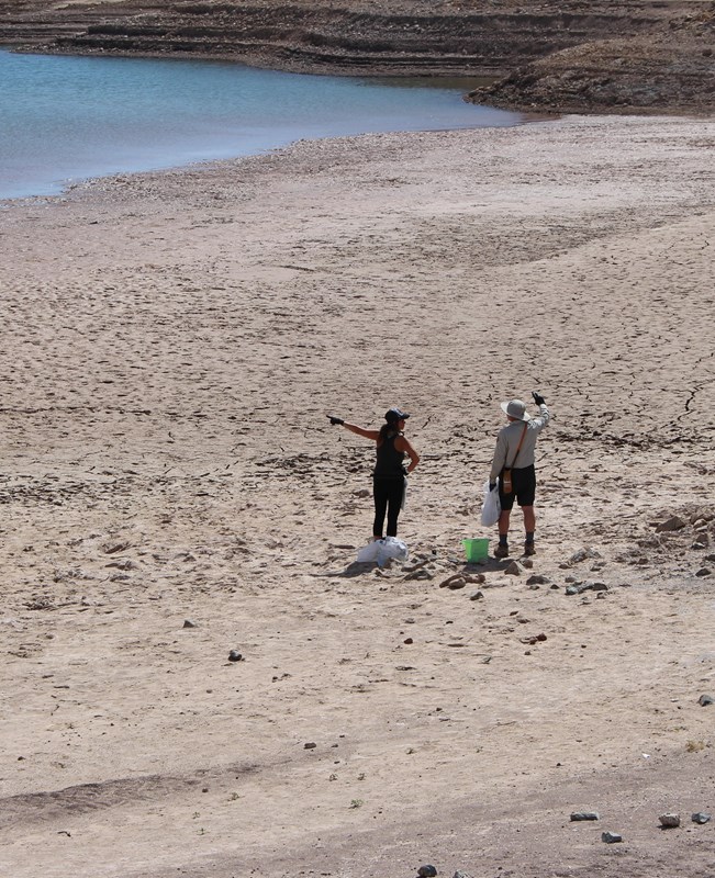 Two volunteers with litter cleanup supplies standing at the shoreline