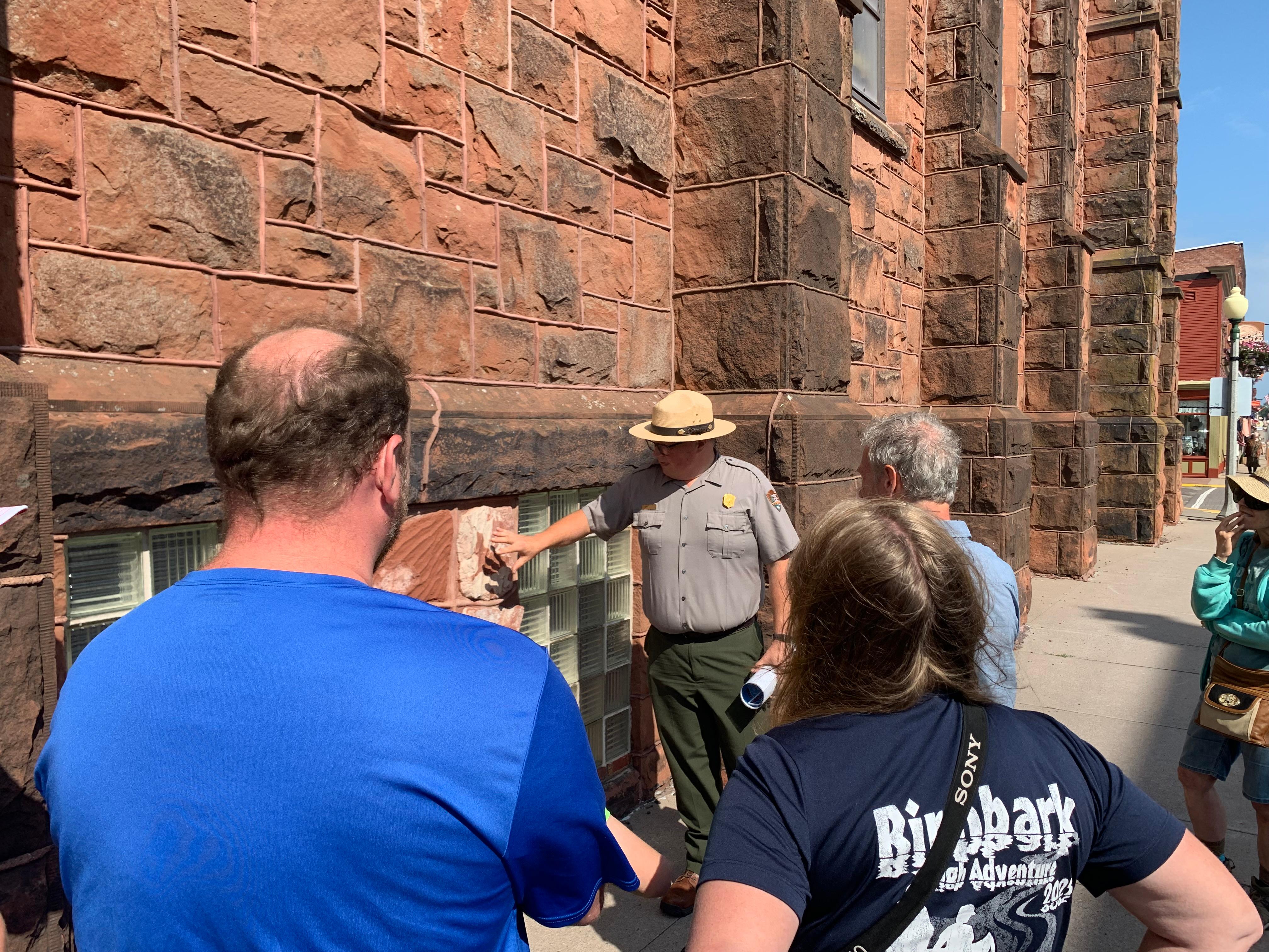 A park ranger points out sandstone on a large building to a group of visitors.