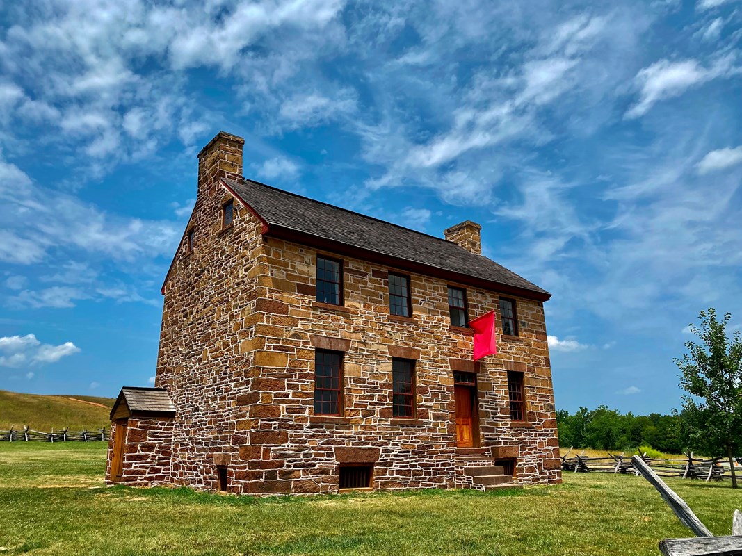A stone two story house with red flag flying out of the second story window.