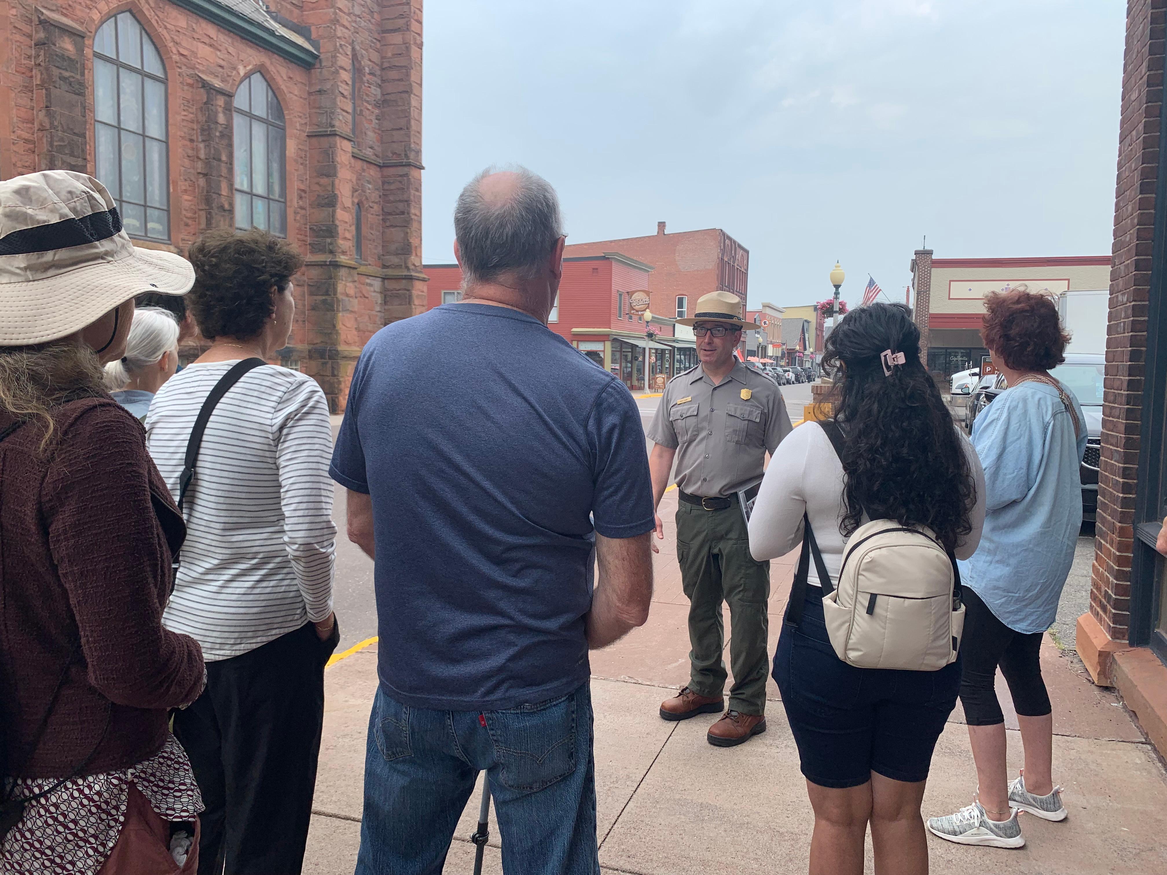 A park ranger talks to a group of people on the sidewalk.