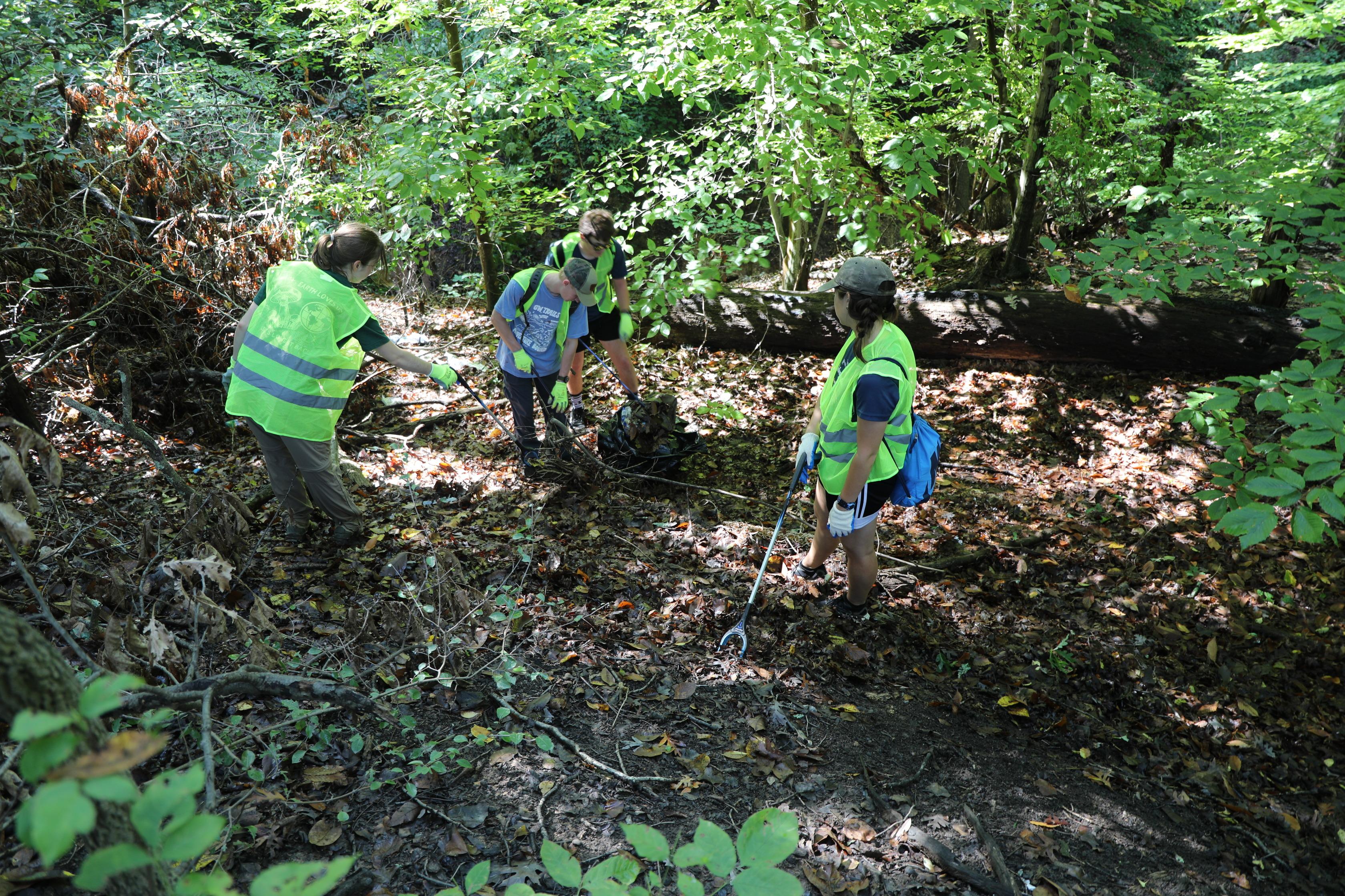 Three volunteers pick up garbage from the forest floor.