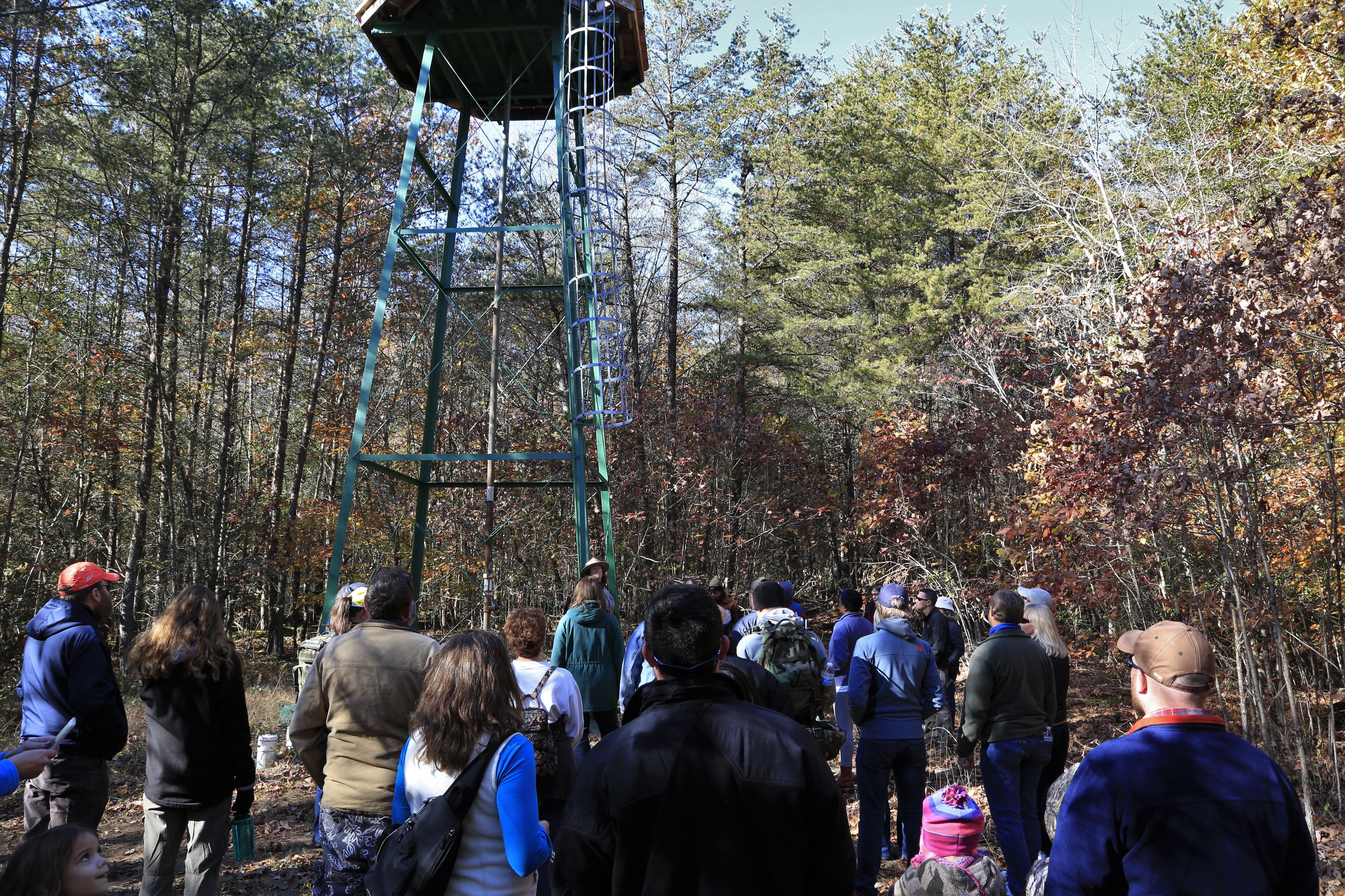 Small group of people stand near a large green metal water tower in the forest