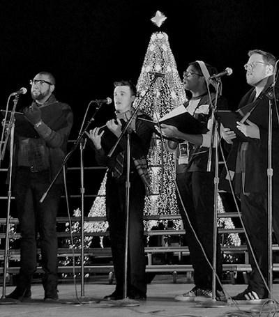 Singers perform in front of a Christmas tree