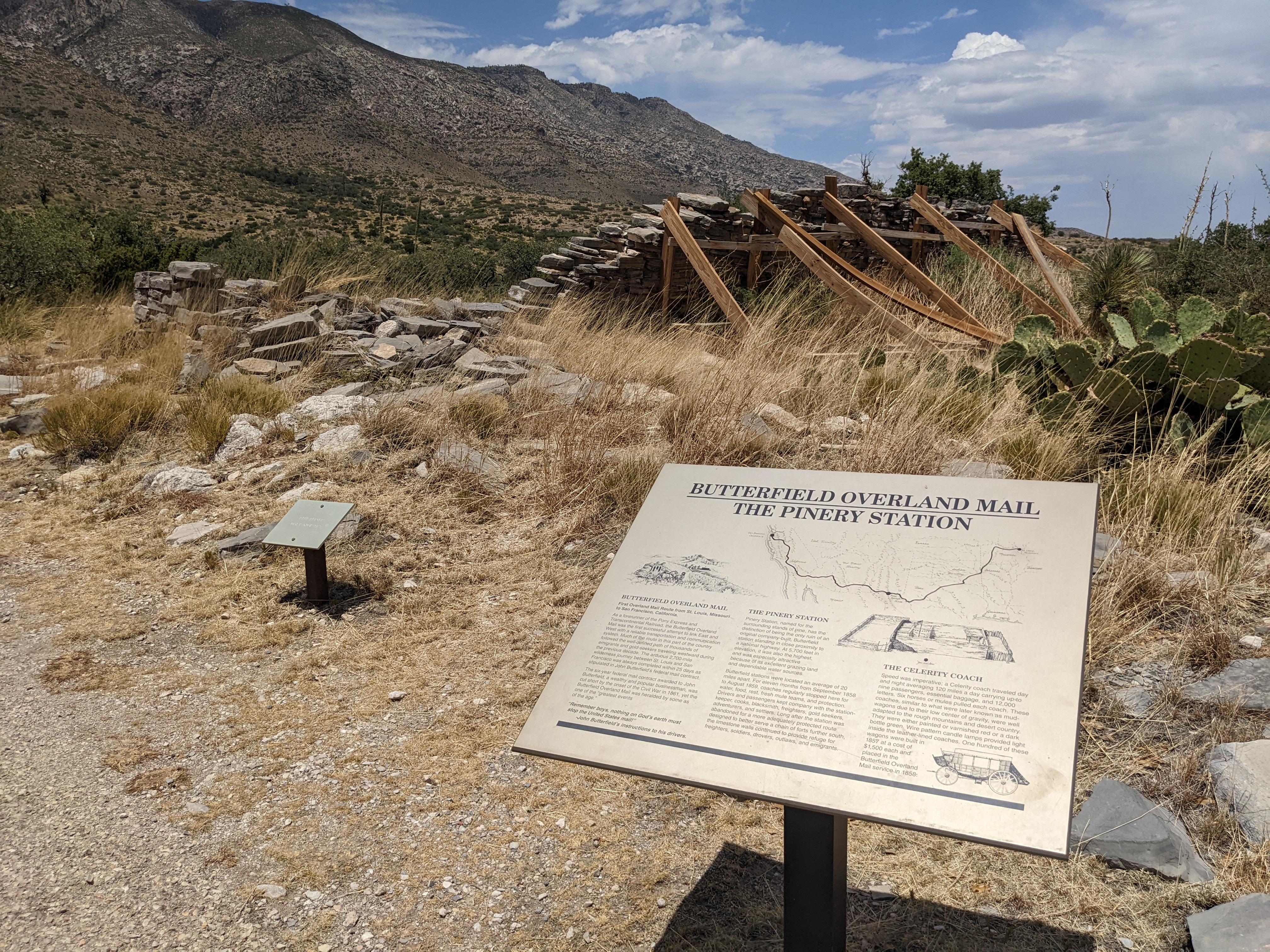 A photo of a sign labeled Ruins of the Pinery Station, with a dilapidated stone wall visible.