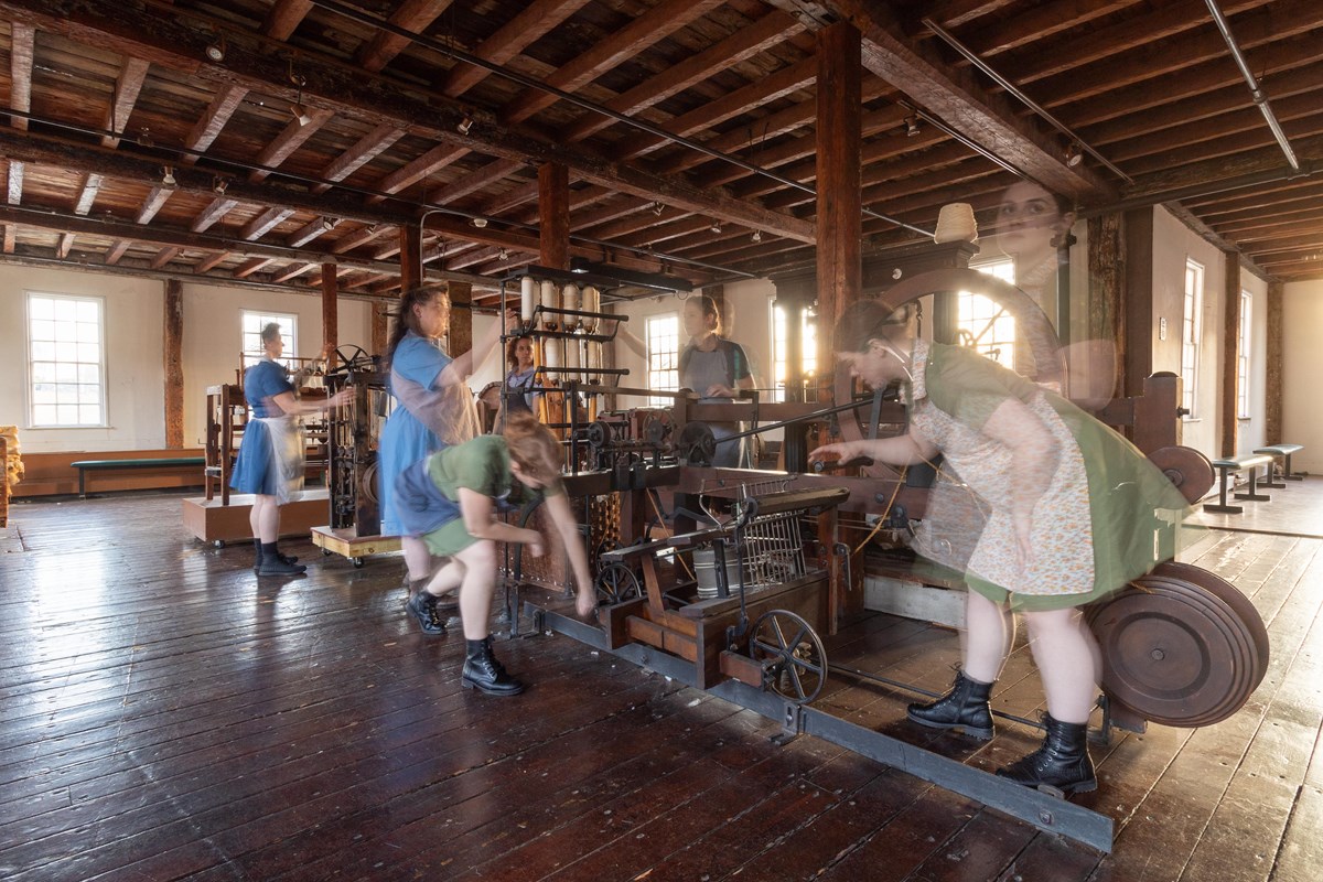 Women dancing between textile machines. The women are transparent and look as if they are moving