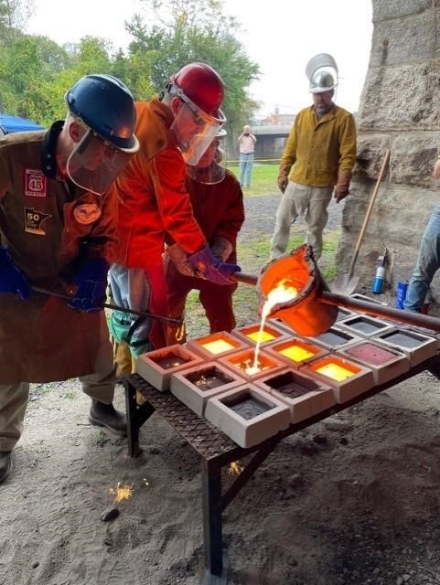 3 individuals working together to pour molten iron into molds