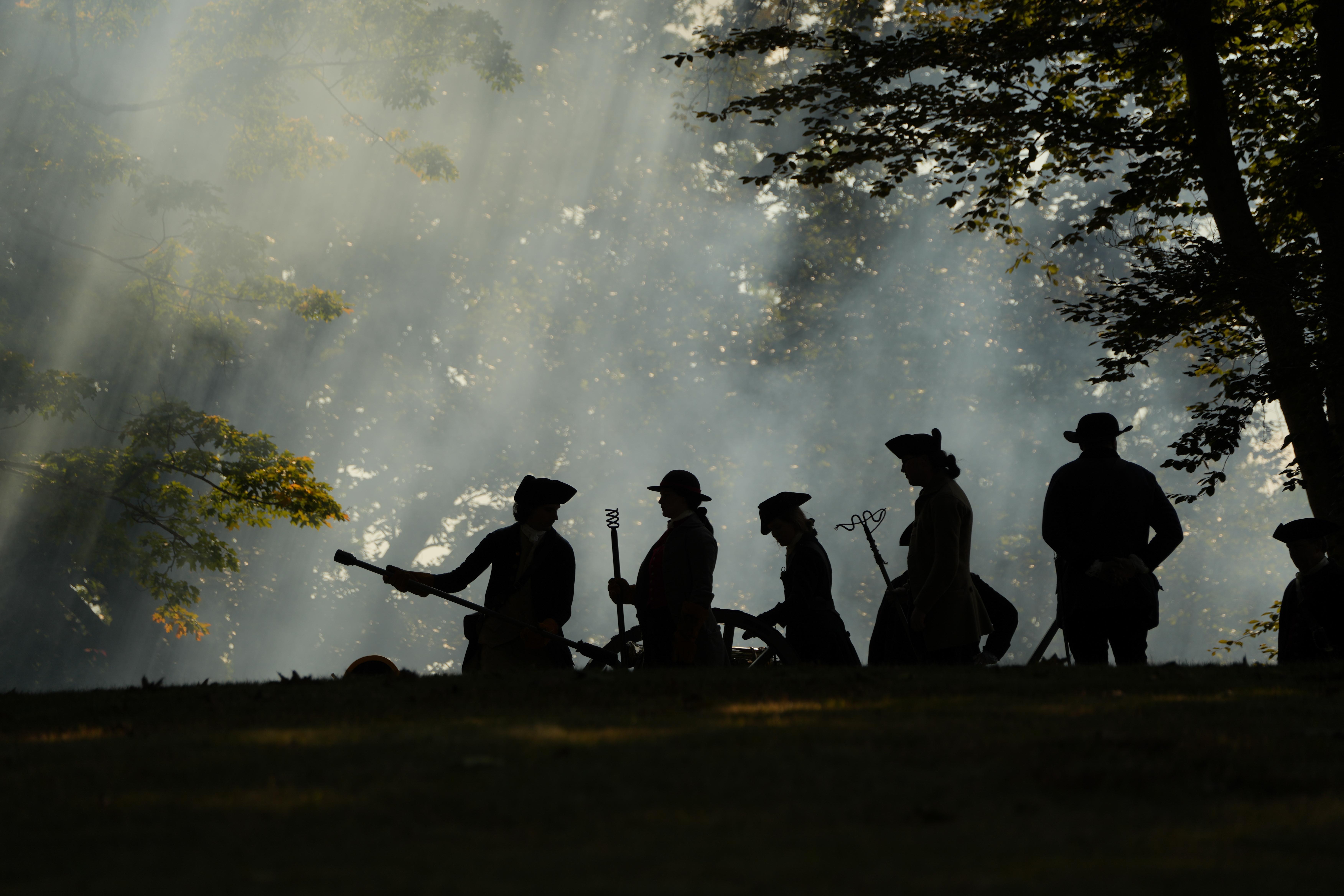 A group of people dressed as Revolutionary War artillery soldiers are working on a cannon