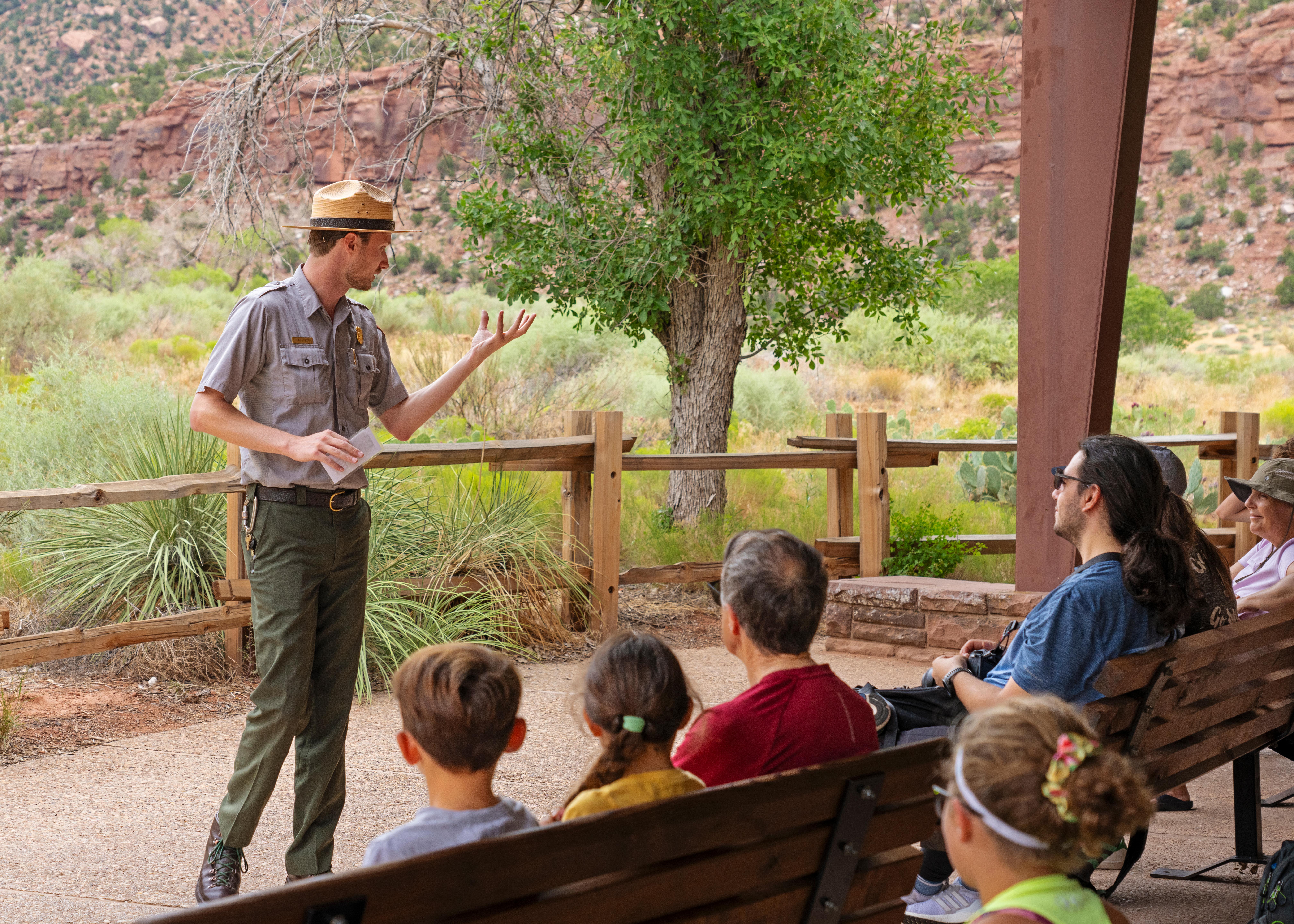 A park ranger stands in front of a crowd of seated visitors on a cement patio.