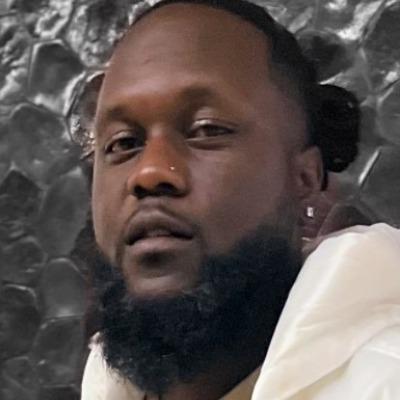 African American man with a beard and nose piercing smiles at camera