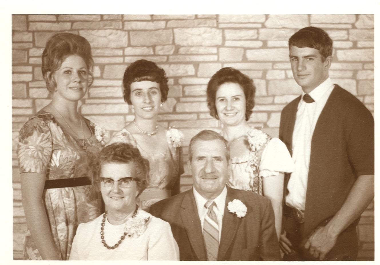 A family photo with a mother and father sitting with their four children standing behind them.