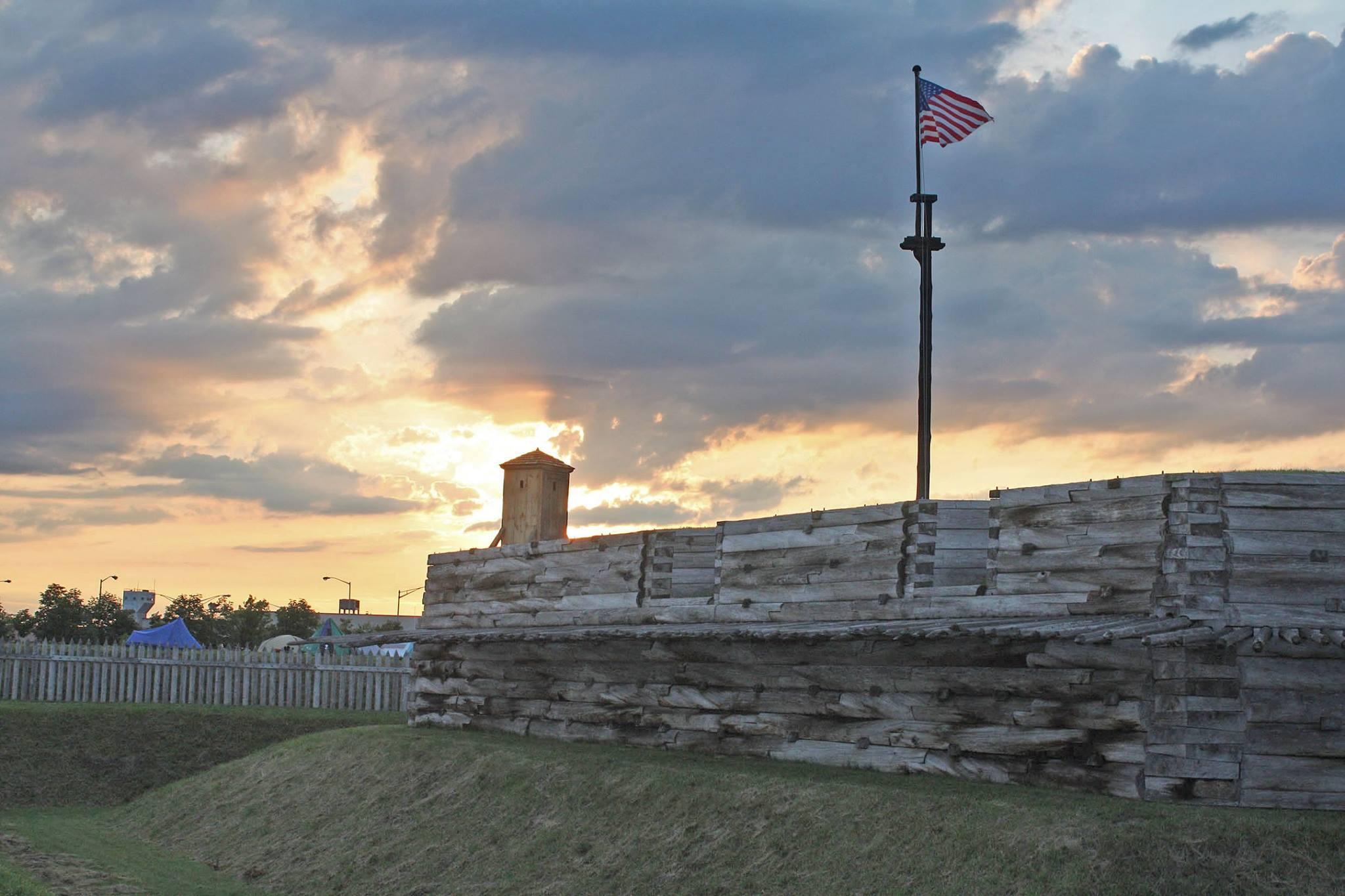 A flag flies over the walls of a wooden fort