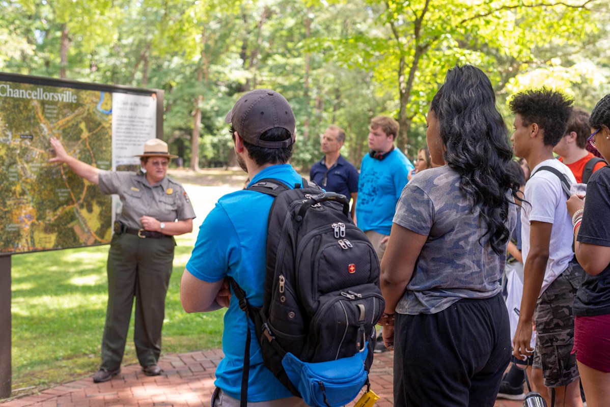 A park ranger points to a battle map as a crowd surrounds her.