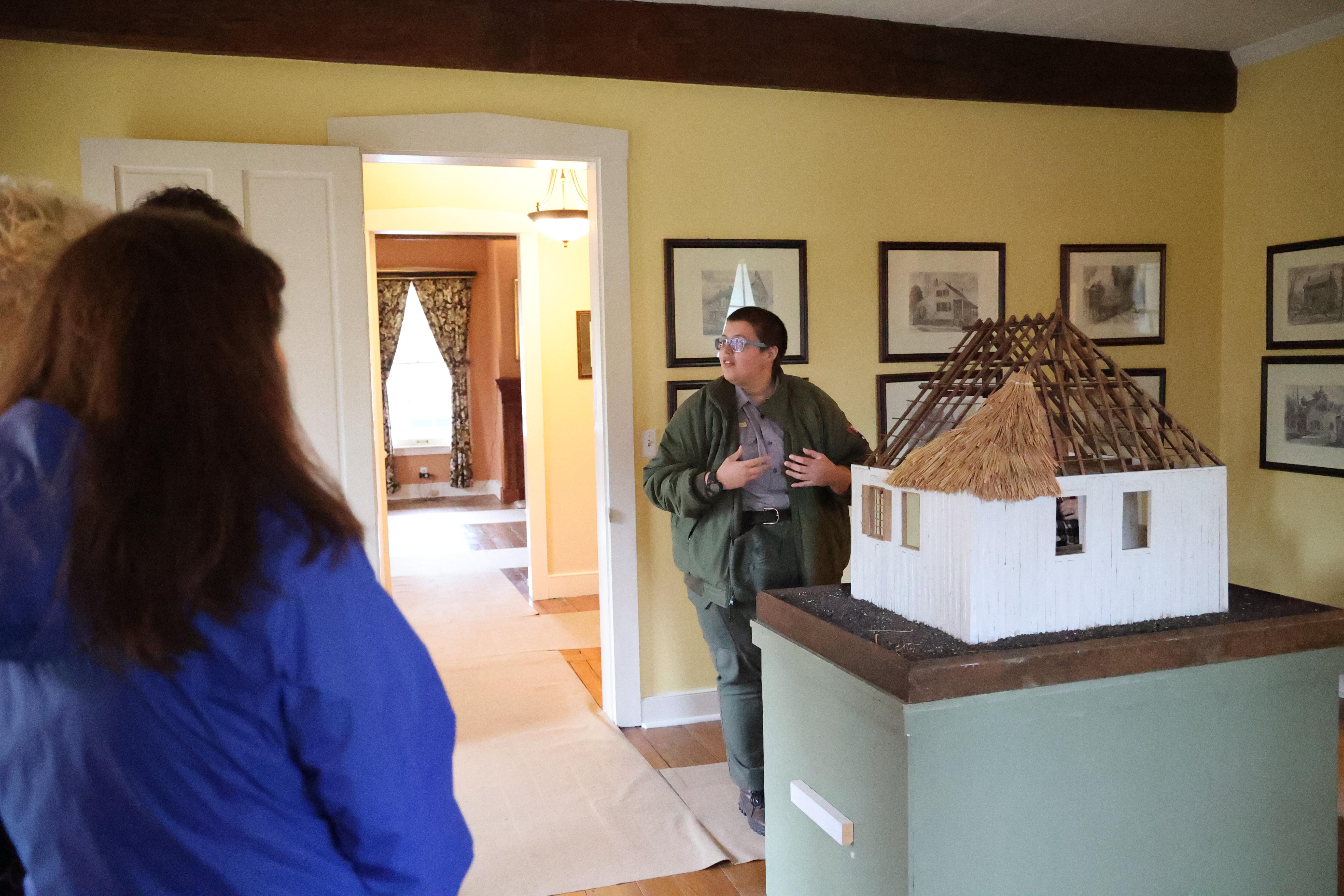 Park ranger stands in front of a yellow wall with sketches hanging on it looking at visitors.