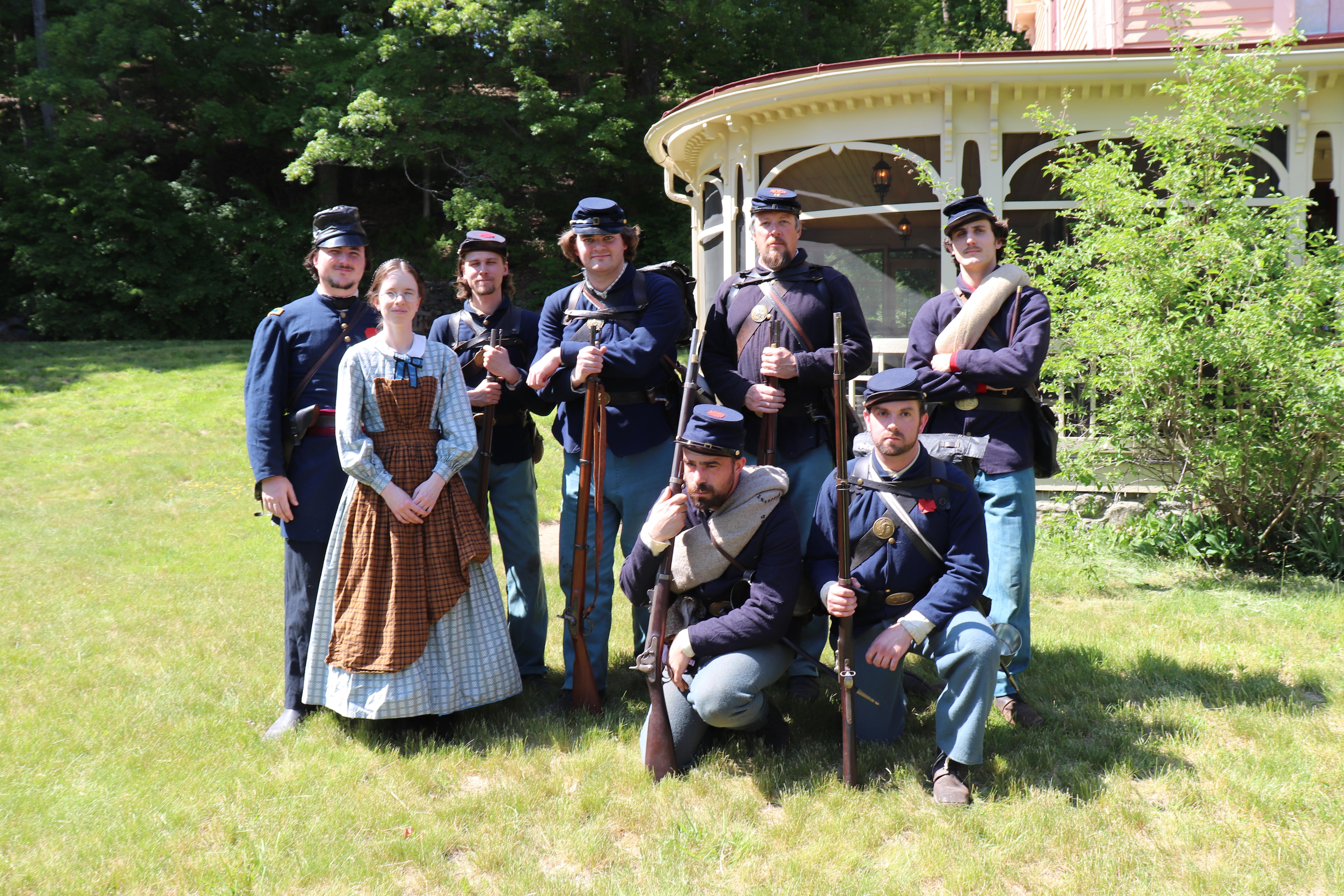 A group of men and women dressed as civil war soldiers and civilians stand outside a historic house