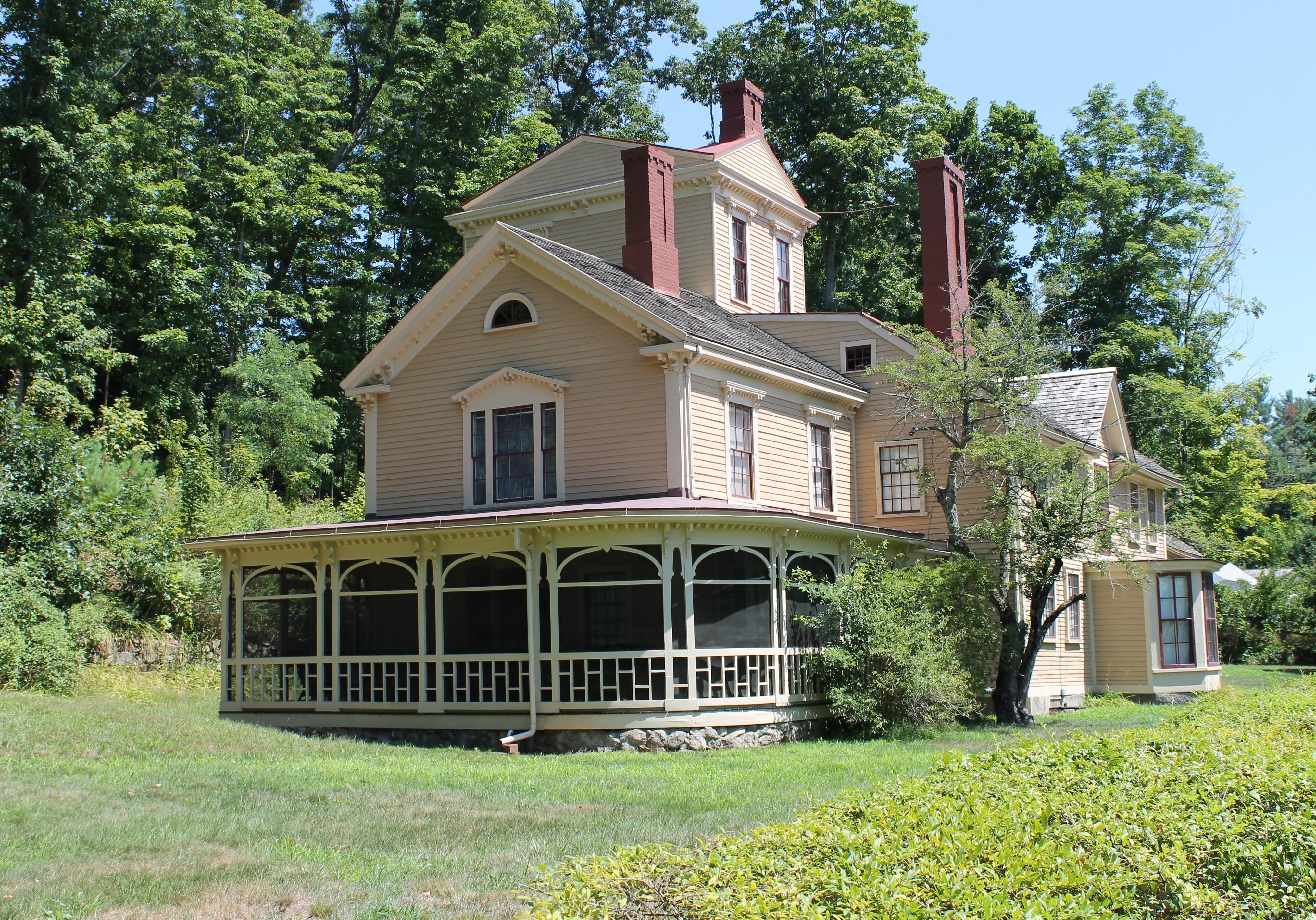 A yellow wooden house with wrap around porch and 3 story central tower