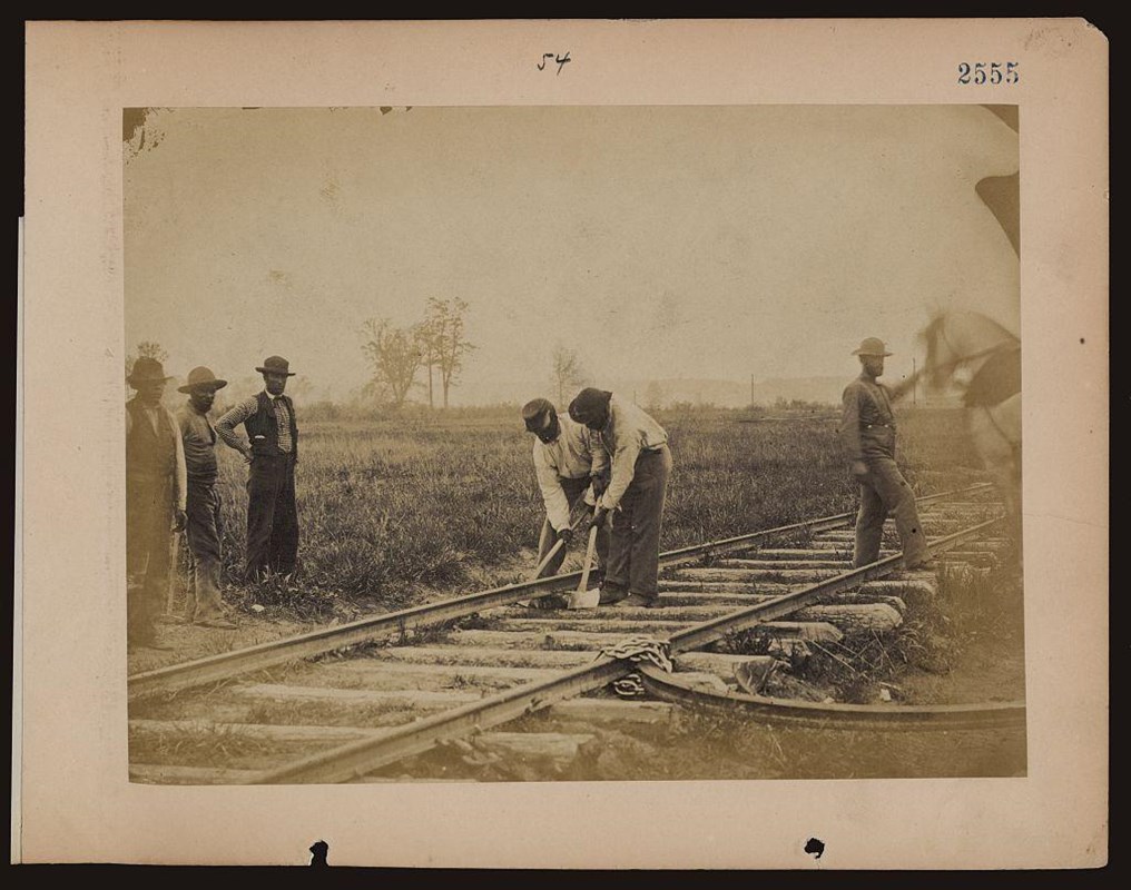 A sepia toned image from 1862/3 of Black men working on a railroad line.