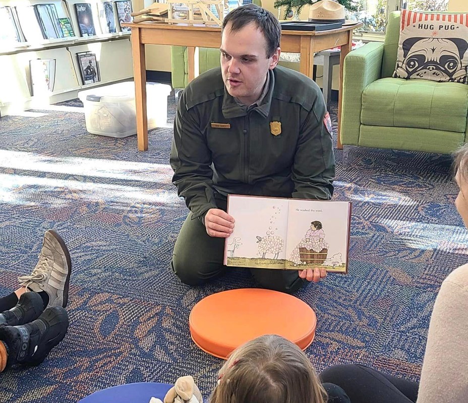 A ranger sitting on the floor and reading a story to a group of children.