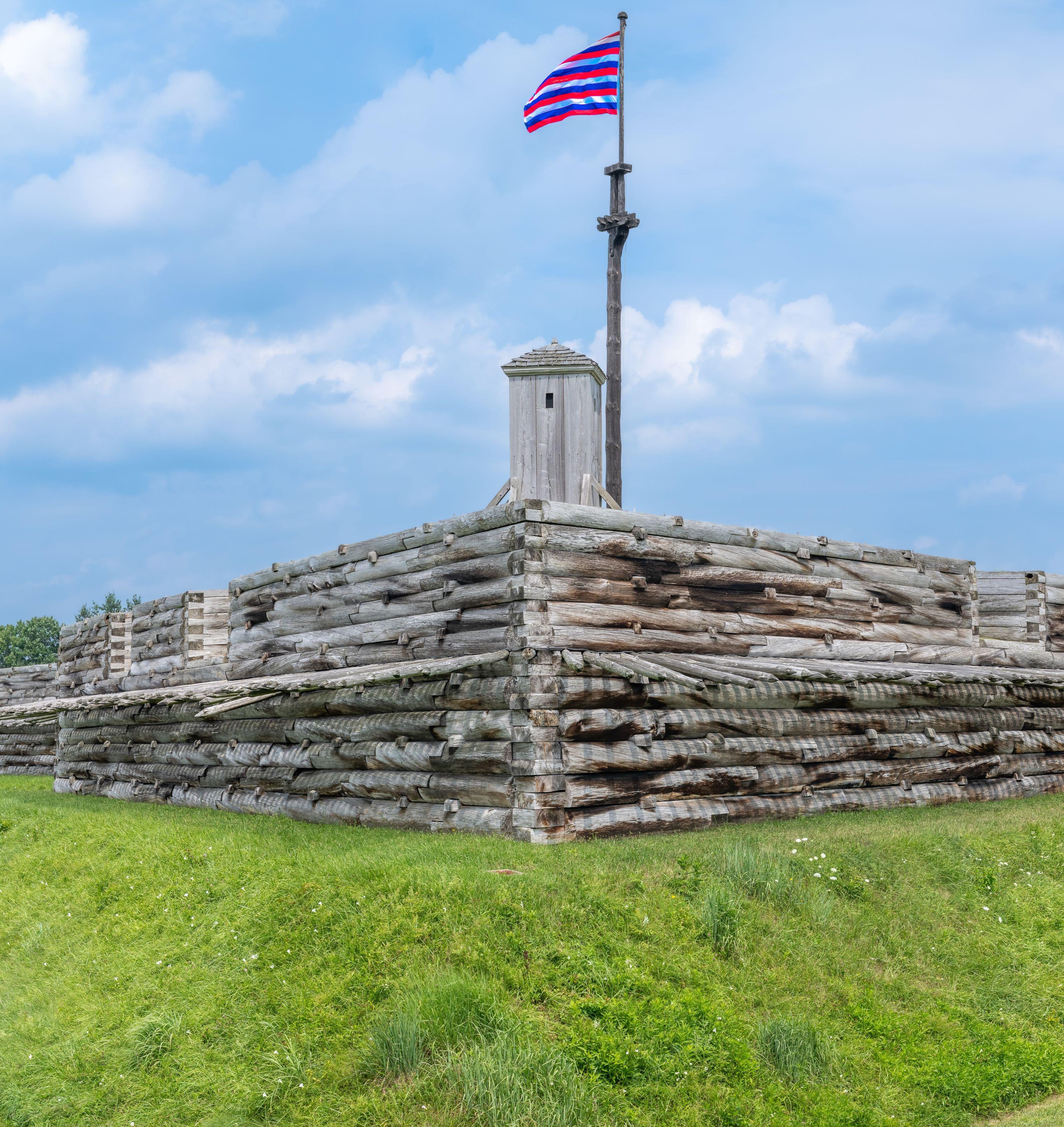 A vibrant flag waves over the walls of a wooden fort.