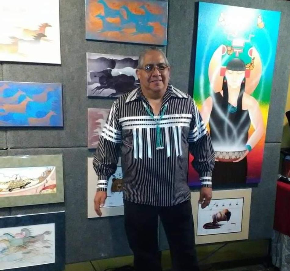 A portrait of a man standing in front of colorful paintings.