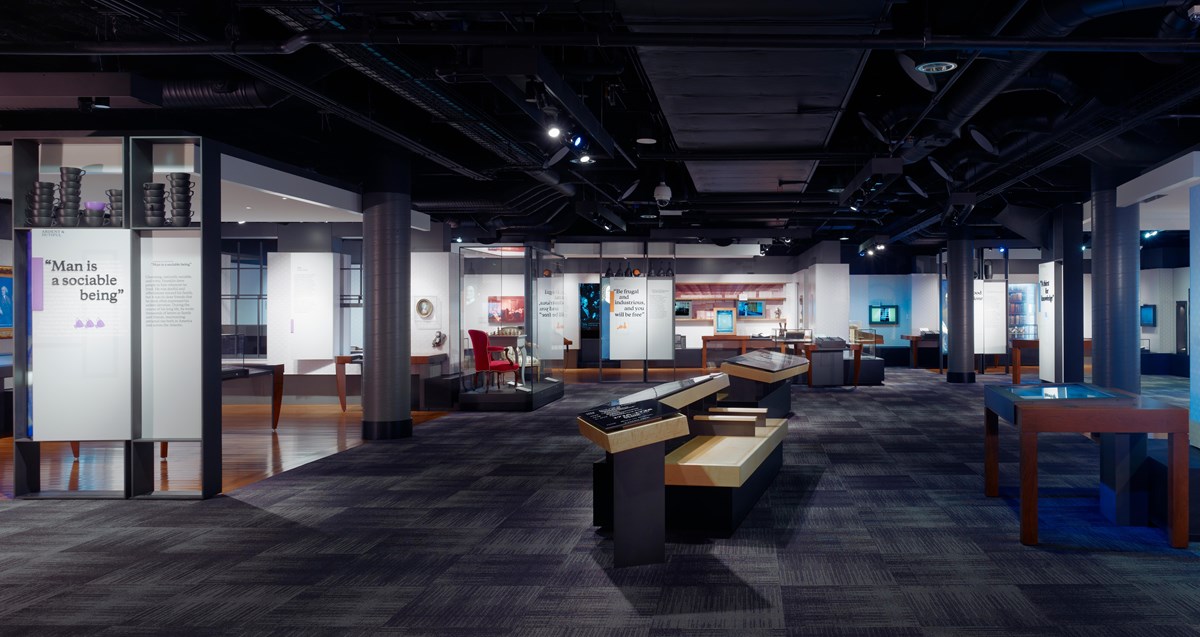 Multiple exhibit panels with text and images surround benches centered in the middle of the room.