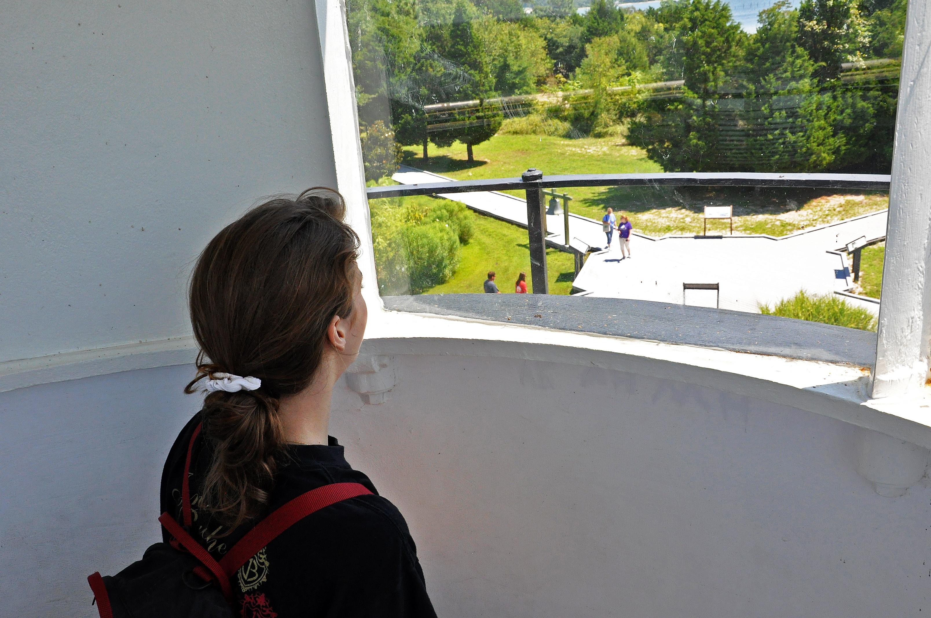View from inside a lighthouse with a person looking out at a green landscape and pathway.