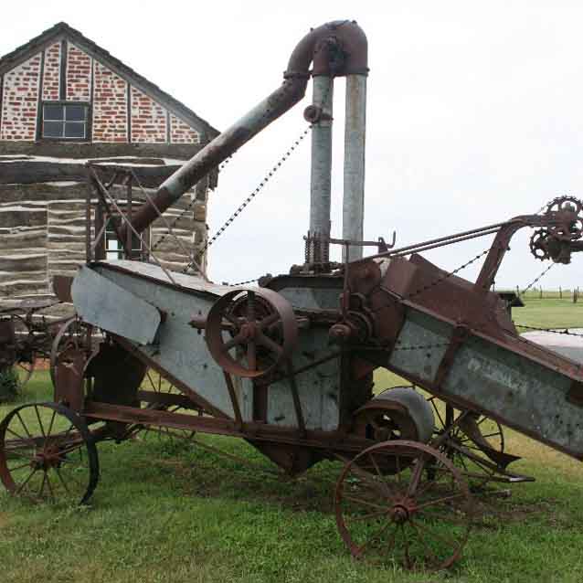 A farm implement rests in the grass by a homesteading cabin A farm implement rests in the grass by a homesteading cabin