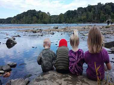 Children sitting on rocks near shore of waterway Children sitting on rocks near shore of waterway