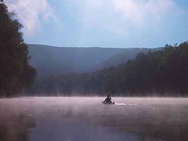 Kayaker travels through misty water with mountains around waterway Kayaker travels through misty water with mountains around waterway