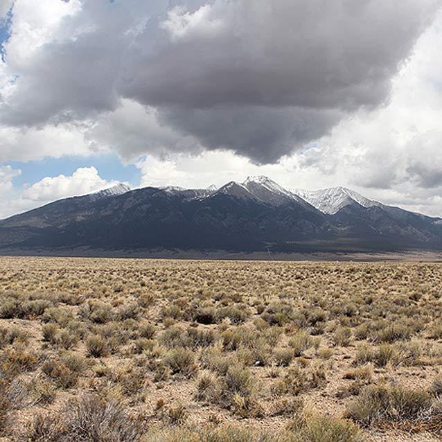 desert scrub in the foreground, spiky mountain range in the background with white clouds desert scrub in the foreground, spiky mountain range in the background with white clouds
