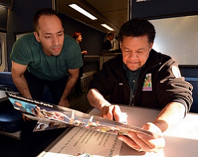 A seated volunteer helps a train passenger find his park on a map on board a passenger train. A seated volunteer helps a train passenger find his park on a map on board a passenger train.